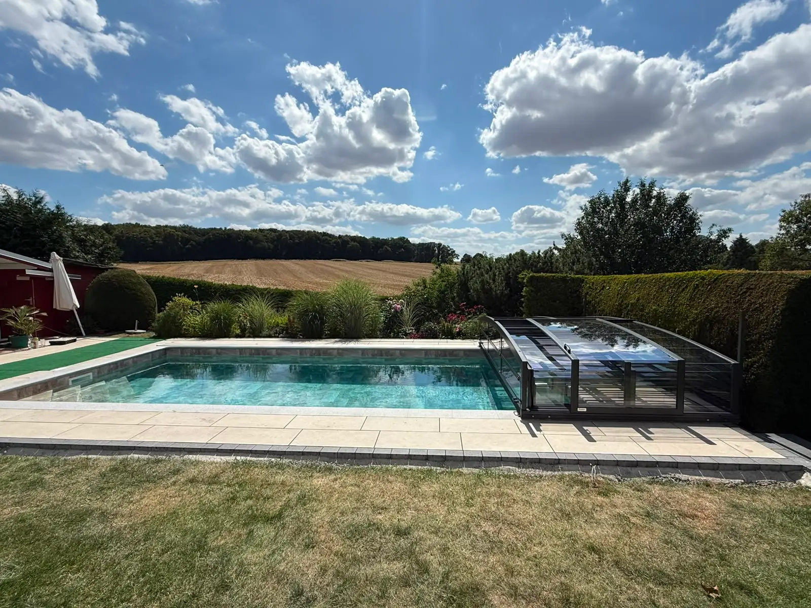 Kundenprojekt von Glocke Pool: Gartenpool mit flacher, zurückgeschobener Poolüberdachung im Spätsommer